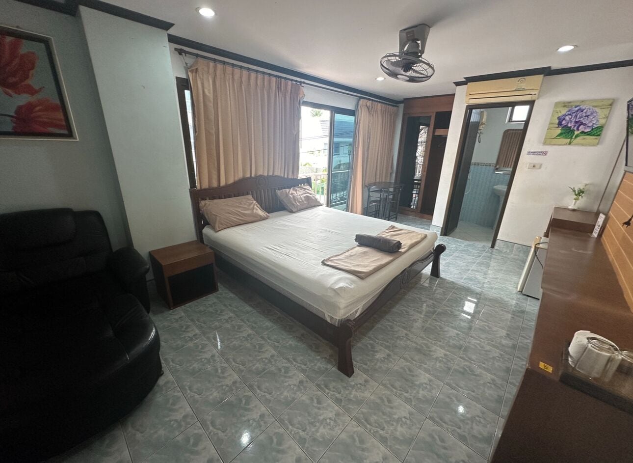 A hotel room with a large bed, a sofa, a small table, and a bathroom visible through an open door.