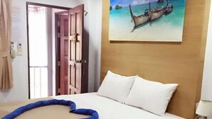 A hotel room with a bed, a painting of boats on water, a wooden headboard, and a nightstand with a lamp. - BAAN KETKAEW GUEST HOUSE 2 (Patong)