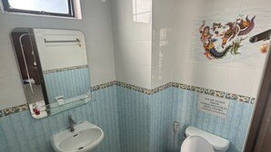 A small bathroom with a sink, toilet, and mirror. The walls are tiled with a blue pattern, and there is a decorative mural on the wall. - BAAN KETKAEW GUEST HOUSE 2 (Patong)