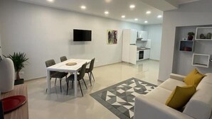 A modern living room with a dining area, a kitchen in the background, and a flat-screen TV mounted on the wall. - Apartment "ALFA" (Rho)