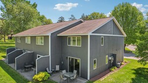 A modern two-story building with a flat roof, a covered patio with a table and chairs, and a small garden area. - Peyton's Place at Tamarack - Great Location! (Wisconsin Dells)