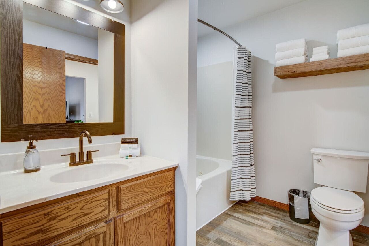 Une salle de bain avec un meuble-lavabo en bois, une baignoire, un rideau de douche et des toilettes.