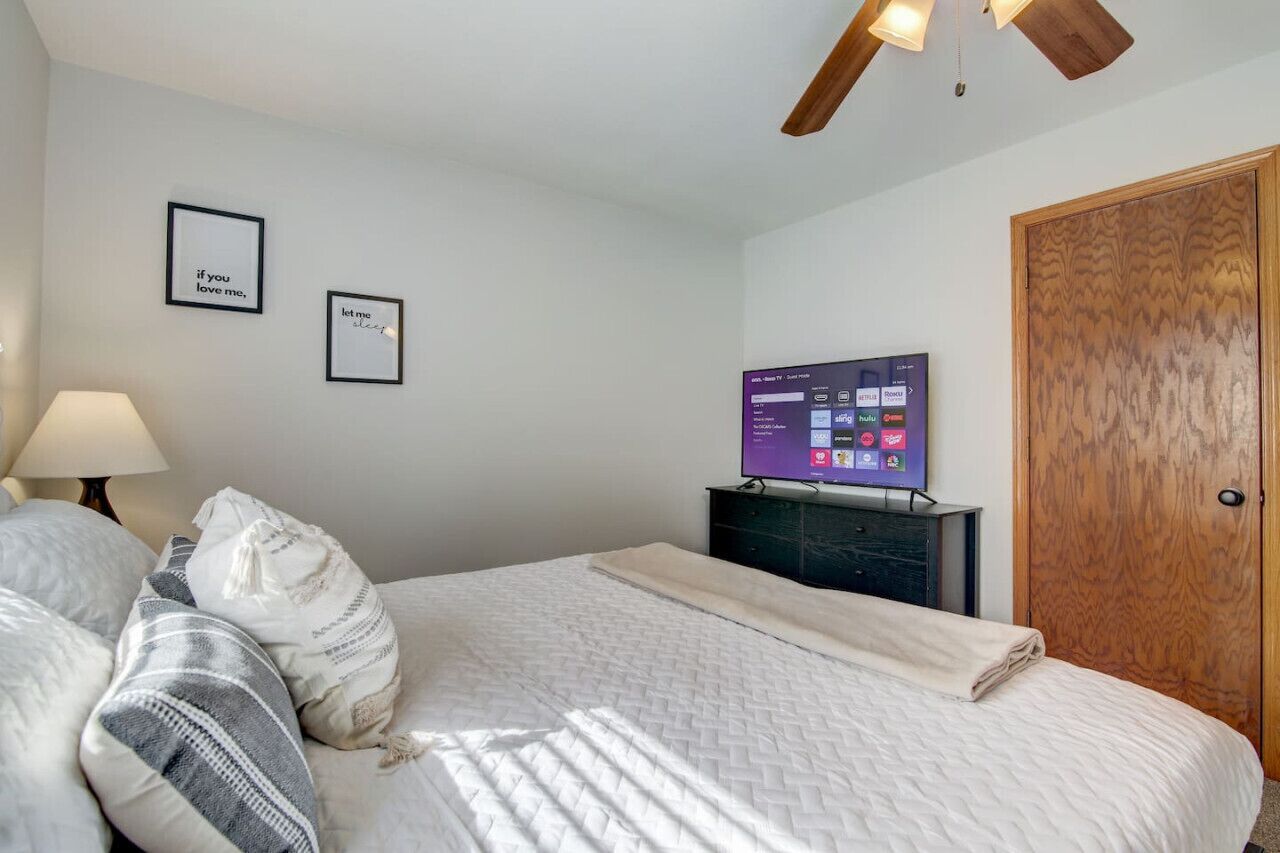 Une chambre à coucher avec un lit, un téléviseur posé sur un meuble, une porte en bois et deux tableaux encadrés accrochés au mur.
