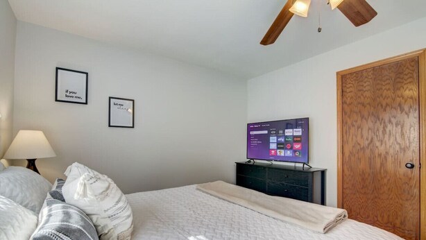 A bedroom with a bed, a television on a stand, a wooden door, and two framed pictures on the wall. - Peyton's Place at Tamarack - Great Location! (Wisconsin Dells)