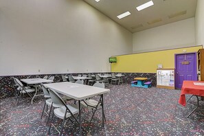A conference room with tables and chairs, a projector screen, and a door with a purple frame. - Peyton's Place at Tamarack - Great Location! (Wisconsin Dells)
