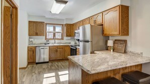A kitchen with wooden cabinets, a stainless steel refrigerator, a marble countertop, and a sign that reads 'Welcome to Peyton's Place.' - Peyton's Place at Tamarack - Great Location! (Wisconsin Dells)