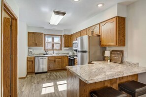 A kitchen with wooden cabinets, a stainless steel refrigerator, a marble countertop, and a sign that reads 'Welcome to Peyton's Place.' - Peyton's Place at Tamarack - Great Location! (Wisconsin Dells)