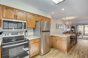 A modern kitchen with wooden cabinets, stainless steel appliances, and a dining area with a view. - Peyton's Place at Tamarack - Great Location! (Wisconsin Dells)