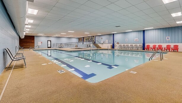 Une piscine intérieure avec des lignes de démarcation bien visibles, un mur en bois et des chaises rouges disposées le long du bord.