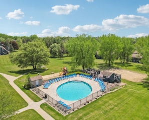 A circular swimming pool with a surrounding deck, a small building, and a playground. - Harrison's Hideaway at Tamarack - Great Location! (Wisconsin Dells)