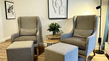 A modern living room with two grey armchairs, a matching ottoman, a small round table with a plant, and a framed 'LOVE' sign on the wall.
