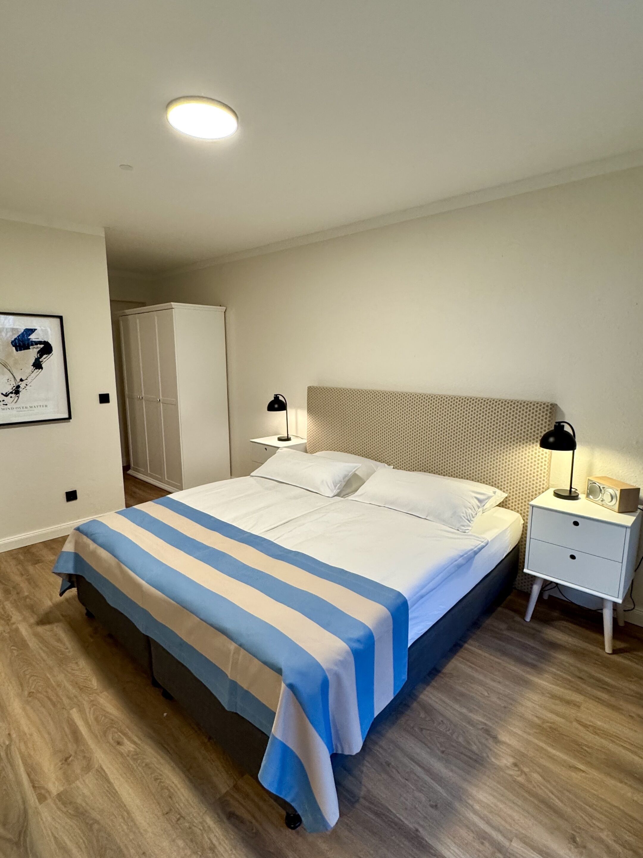 Een keurig opgemaakte slaapkamer met een bed, bedlampen, een nachtkastje en een kledingkast.