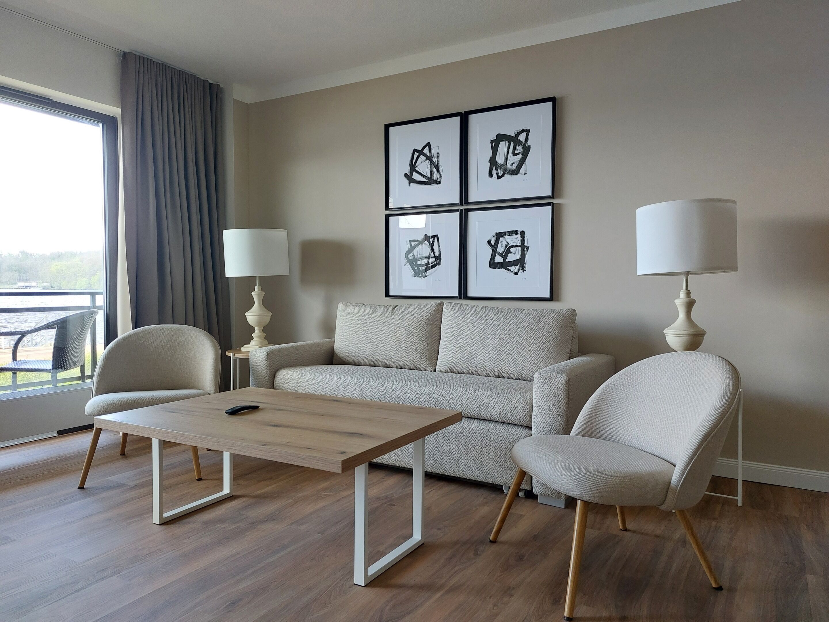A modern living room with a sofa, two armchairs, a coffee table, and two floor lamps. There are framed abstract paintings on the wall.