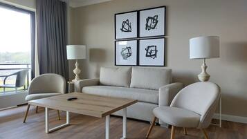 A modern living room with a sofa, two armchairs, a coffee table, and two floor lamps. There are framed abstract paintings on the wall.