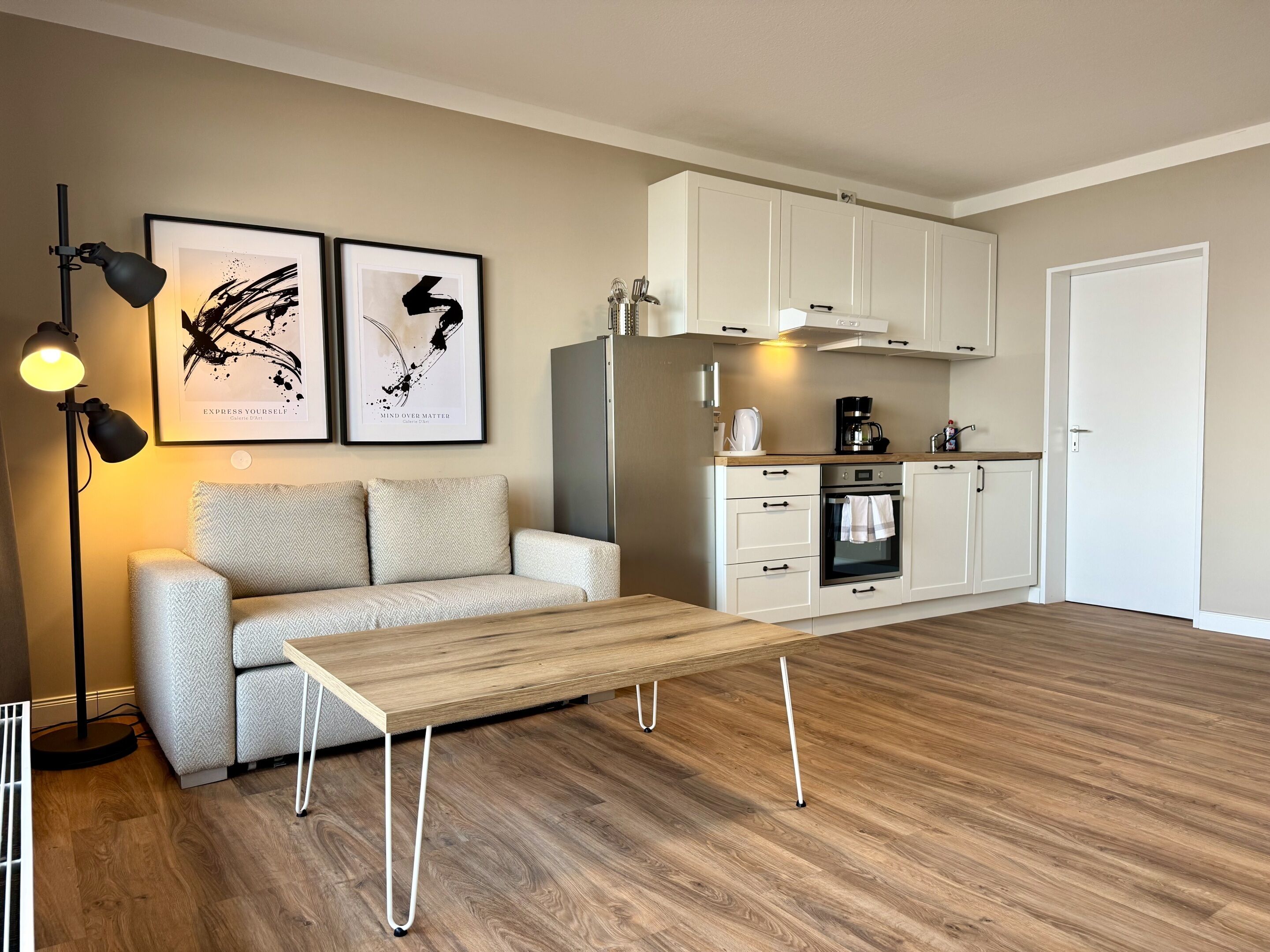 Un salon moderne comprenant un canapé, une table basse et un coin cuisine avec des placards et des appareils électroménagers.