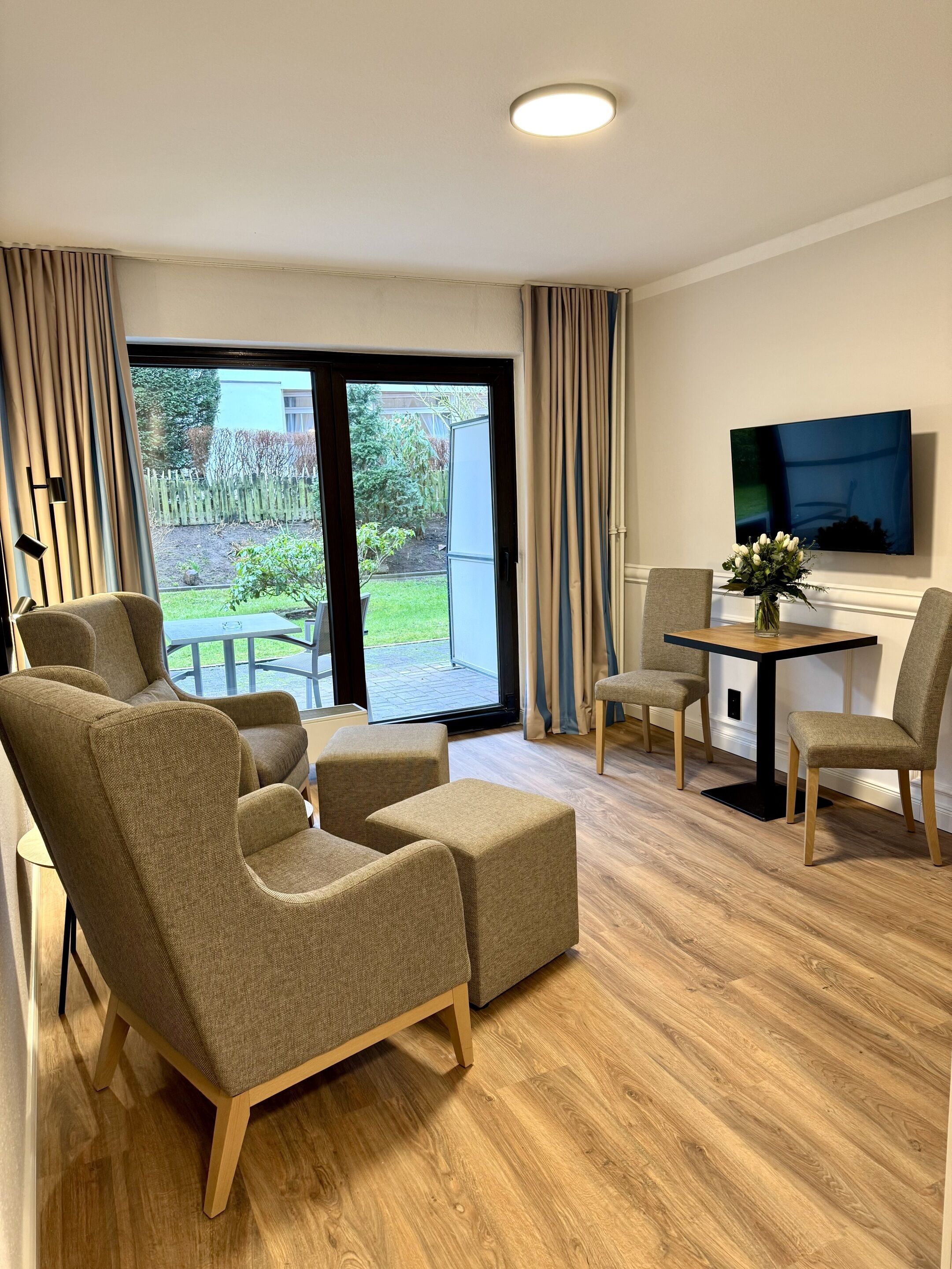 Een moderne woonkamer met een bank, stoelen, een eettafel en een aan de muur bevestigde televisie.
