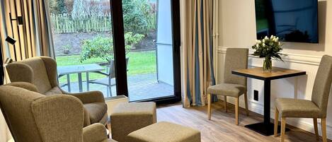 Een moderne woonkamer met een bank, stoelen, een eettafel en een aan de muur bevestigde televisie.