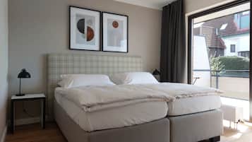 A modern bedroom with a large bed, a bedside table with a lamp, and two framed abstract artworks on the wall.