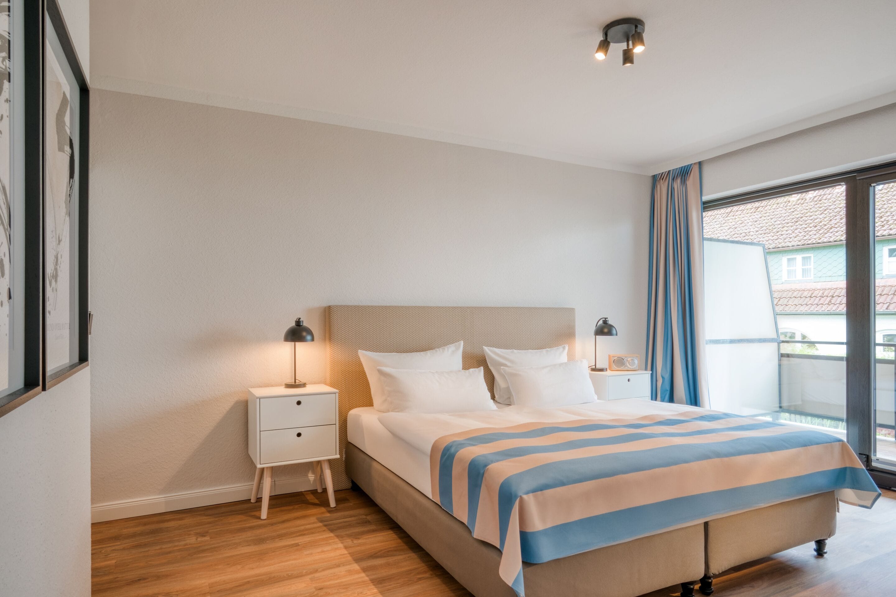Quarto com cama, mesas de cabeceira, cortinas e vista para uma varanda.
