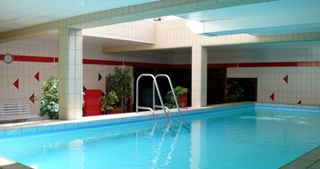 Una piscina interior con escalera, paredes de azulejos y plantas en macetas.