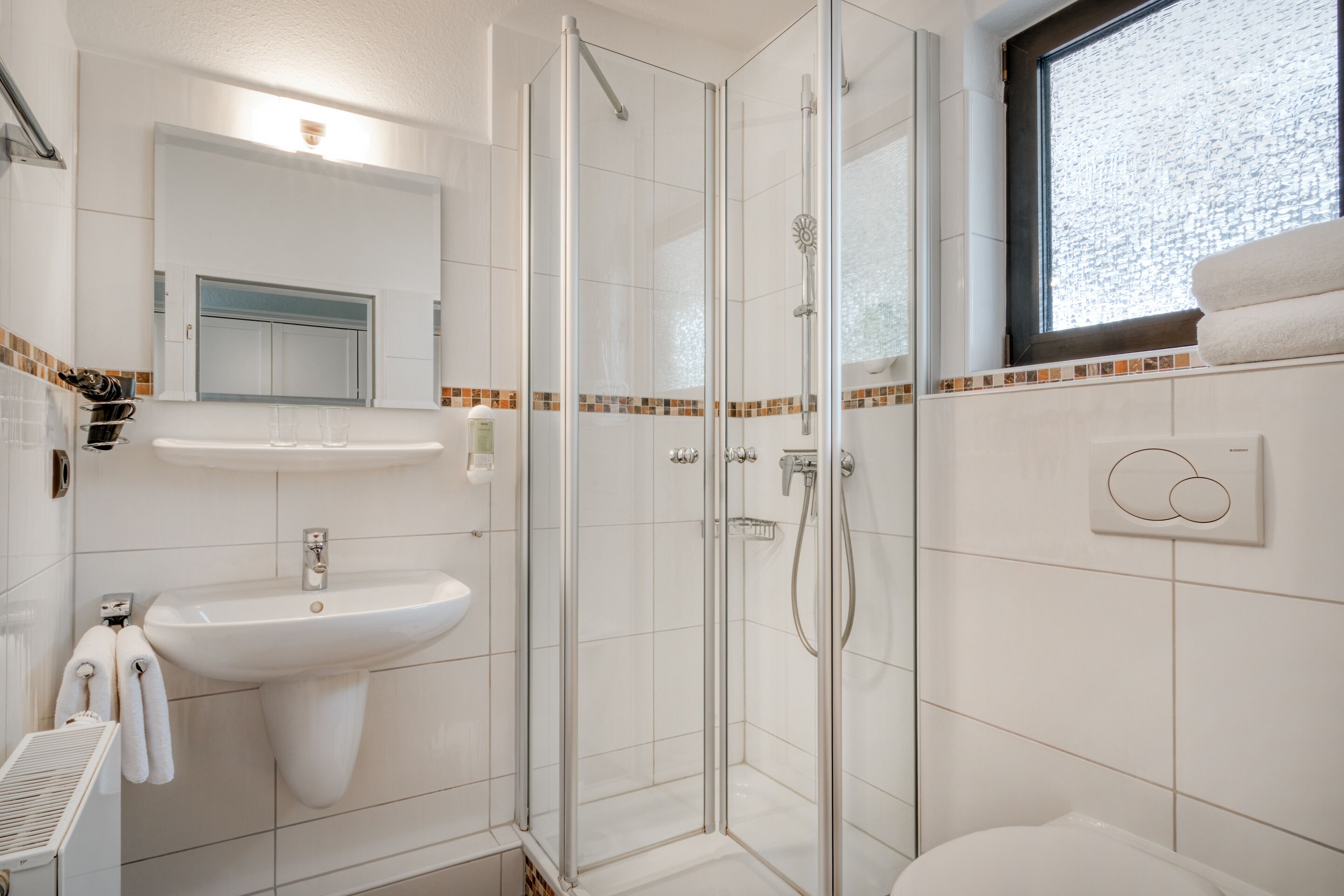 Un baño moderno con ducha de vidrio, un lavabo blanco y una ventana con vistas.
