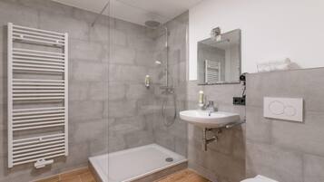 Een moderne badkamer met een douchecabine van glas, een wit wastafelmeubel en een toilet.