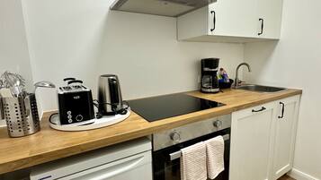 Cocina compacta con gabinetes blancos, encimera de madera, horno integrado y cafetera.