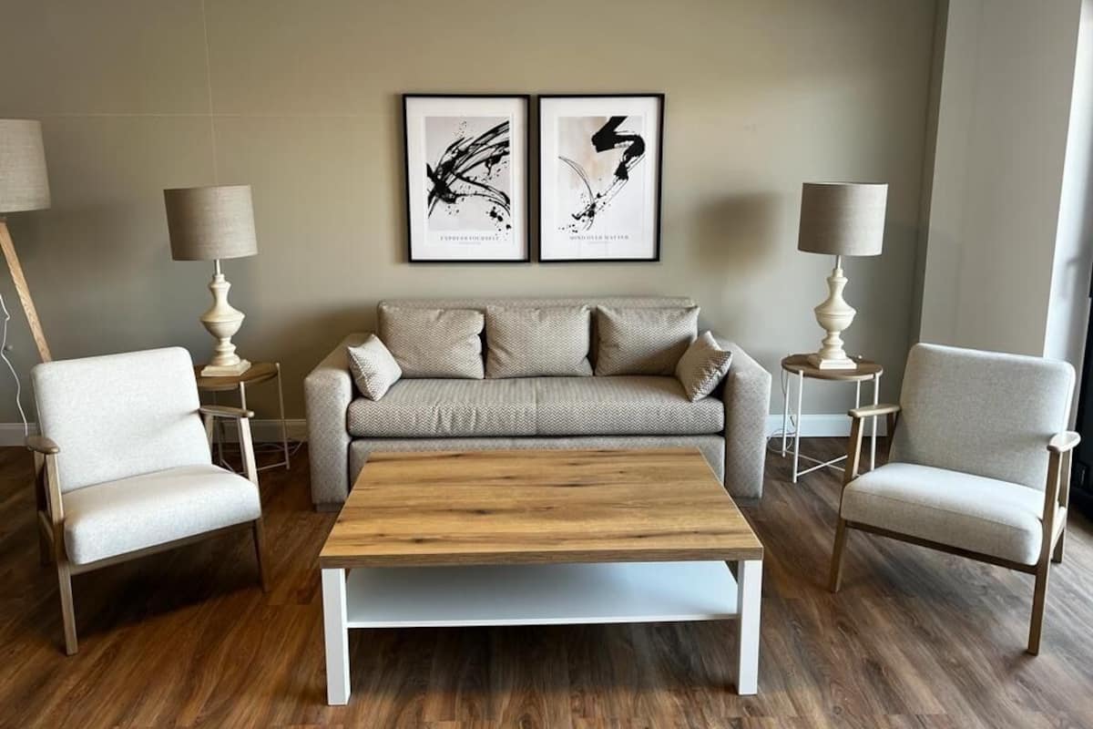 Un salón con un sofá, dos sillones, una mesa de centro y dos lámparas de pie.