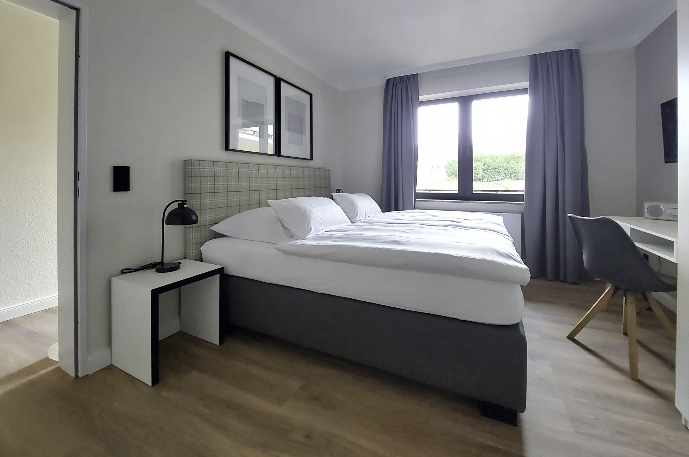A modern hotel room with a large bed, a desk, and a chair.