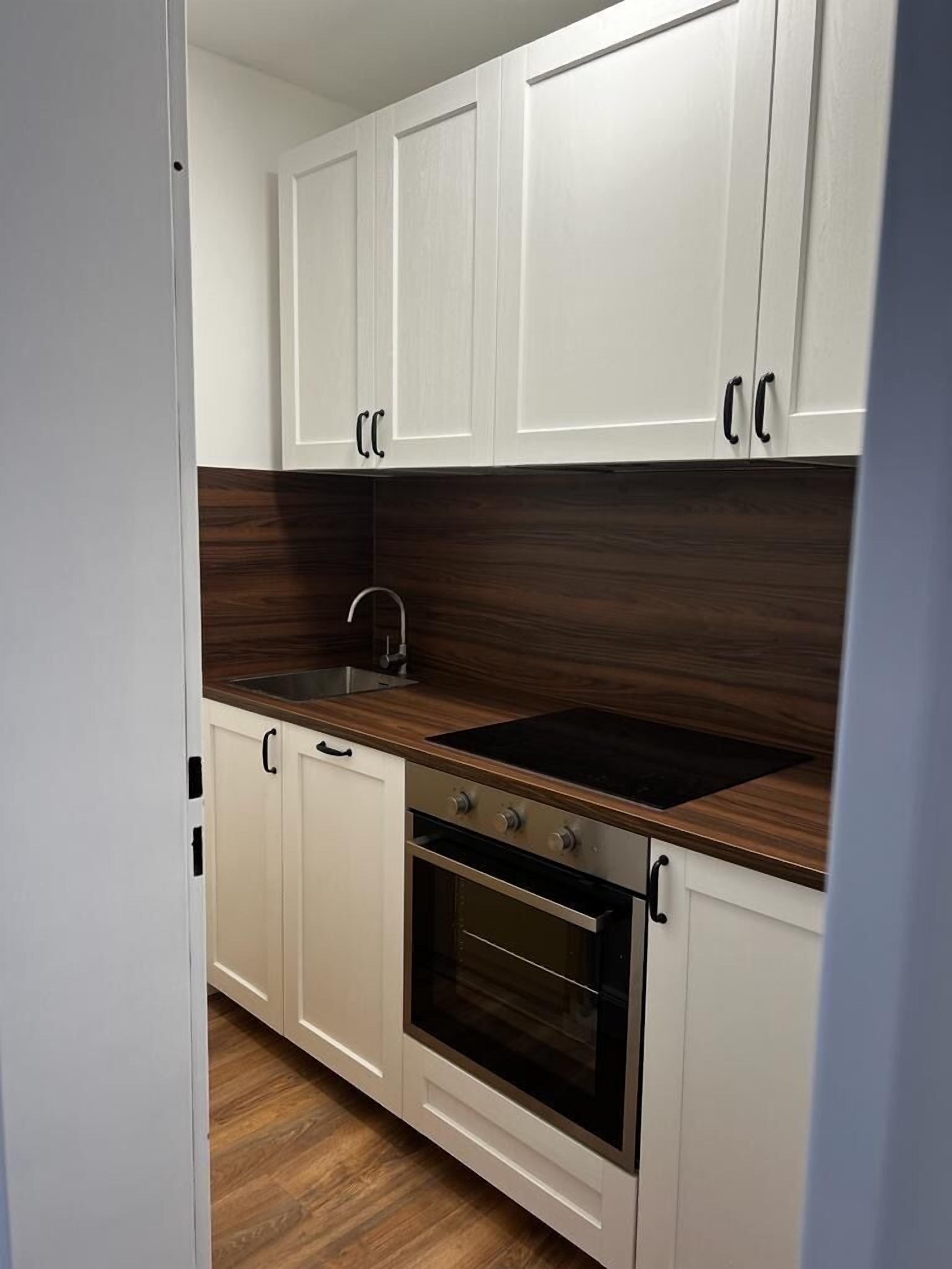 A kitchen with white cabinets, a dark wood countertop, a sink, and an oven.