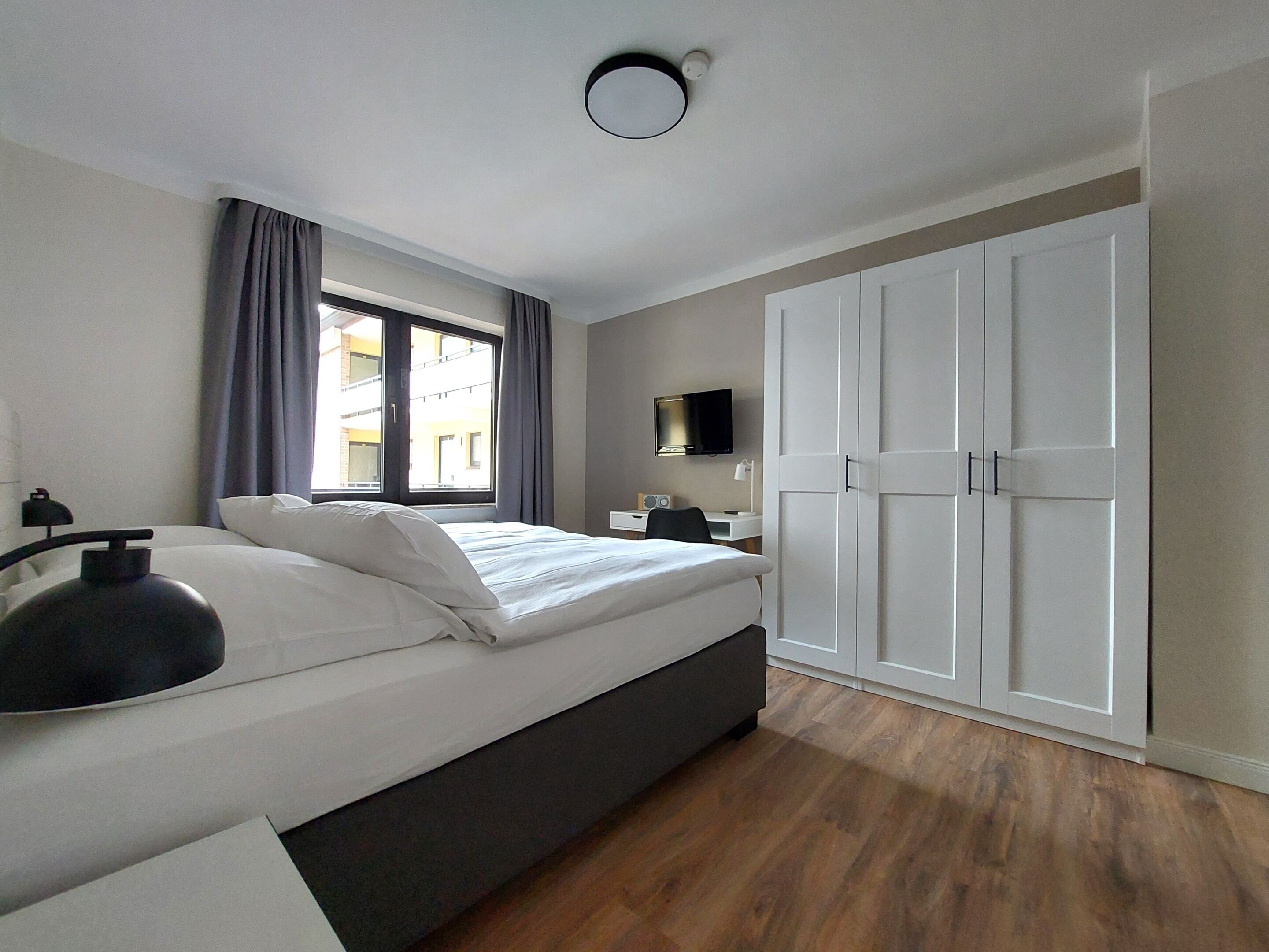 A modern bedroom with a bed, a desk, a TV, and a wardrobe.
