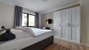 A modern bedroom with a bed, a desk, a TV, and a wardrobe.