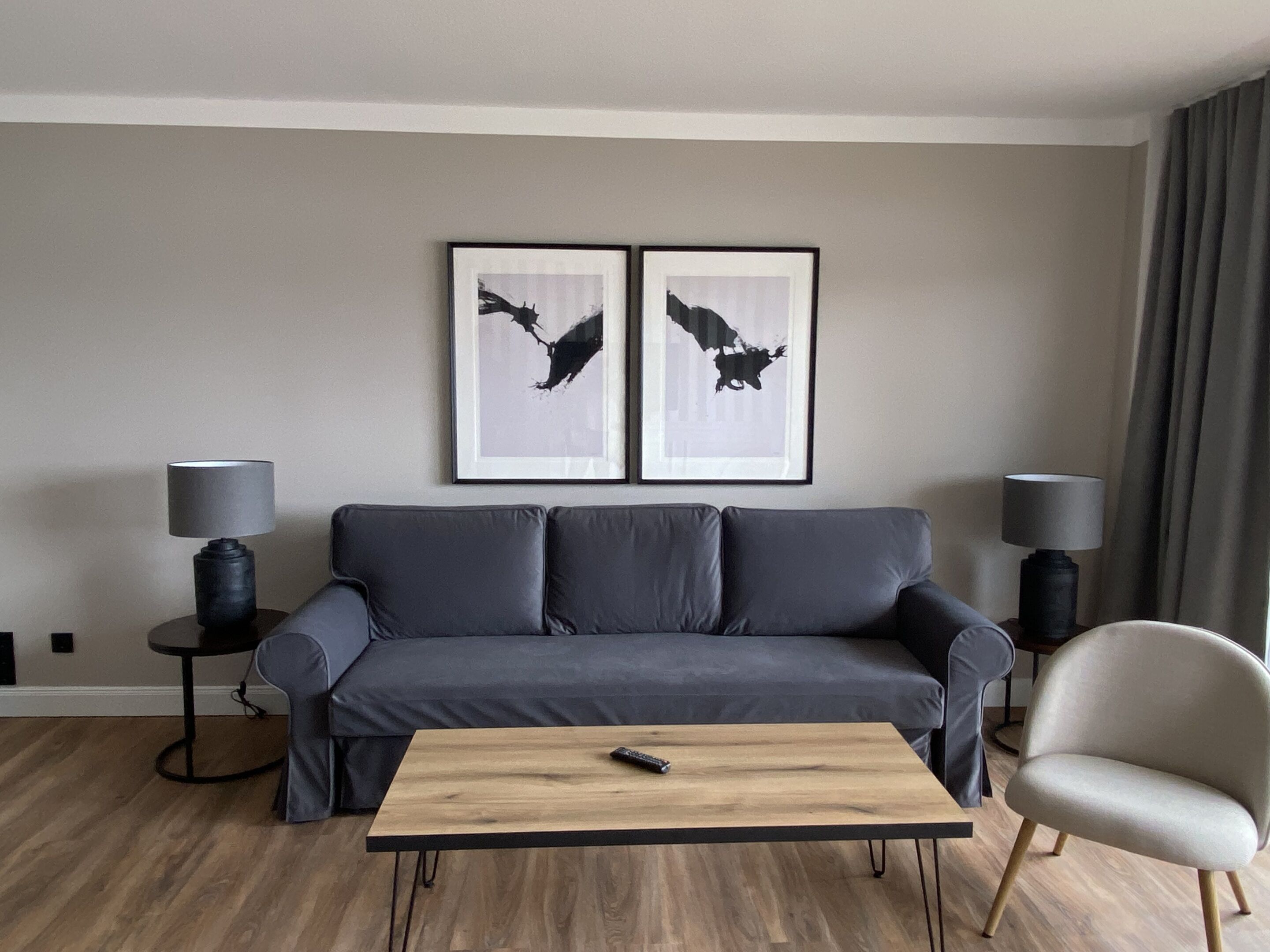 Una sala de estar moderna con un sofá gris, dos lámparas negras, una mesa de centro de madera y dos obras de arte enmarcadas en la pared.