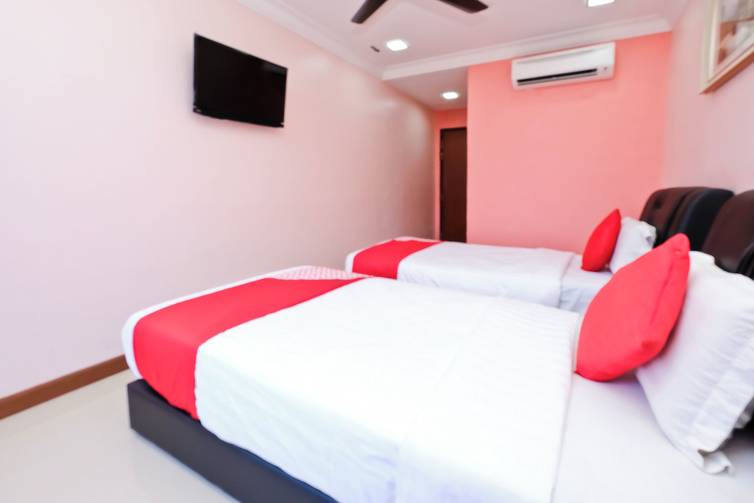 A bedroom with two beds, each with red and white bedding, a flat-screen TV on the wall, and an air conditioning unit.
