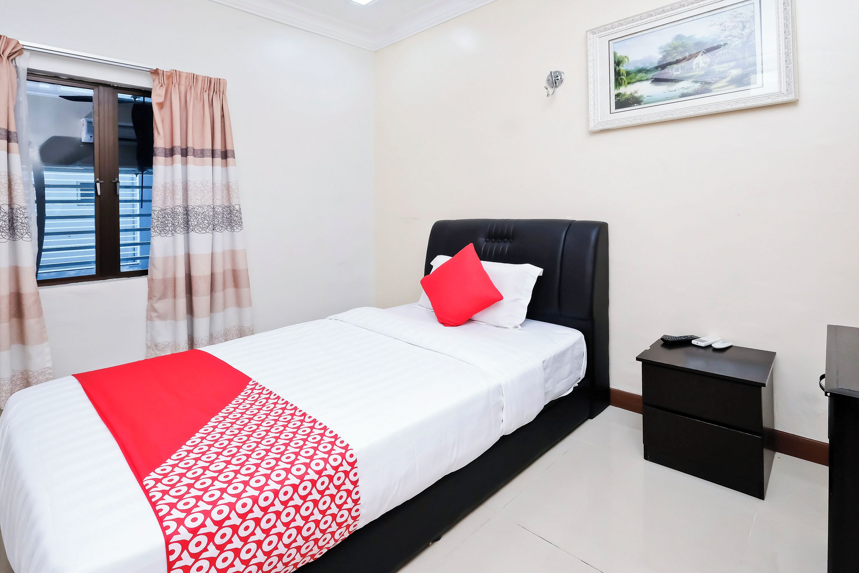 A bedroom with a bed, a nightstand, a window with curtains, and a painting on the wall.