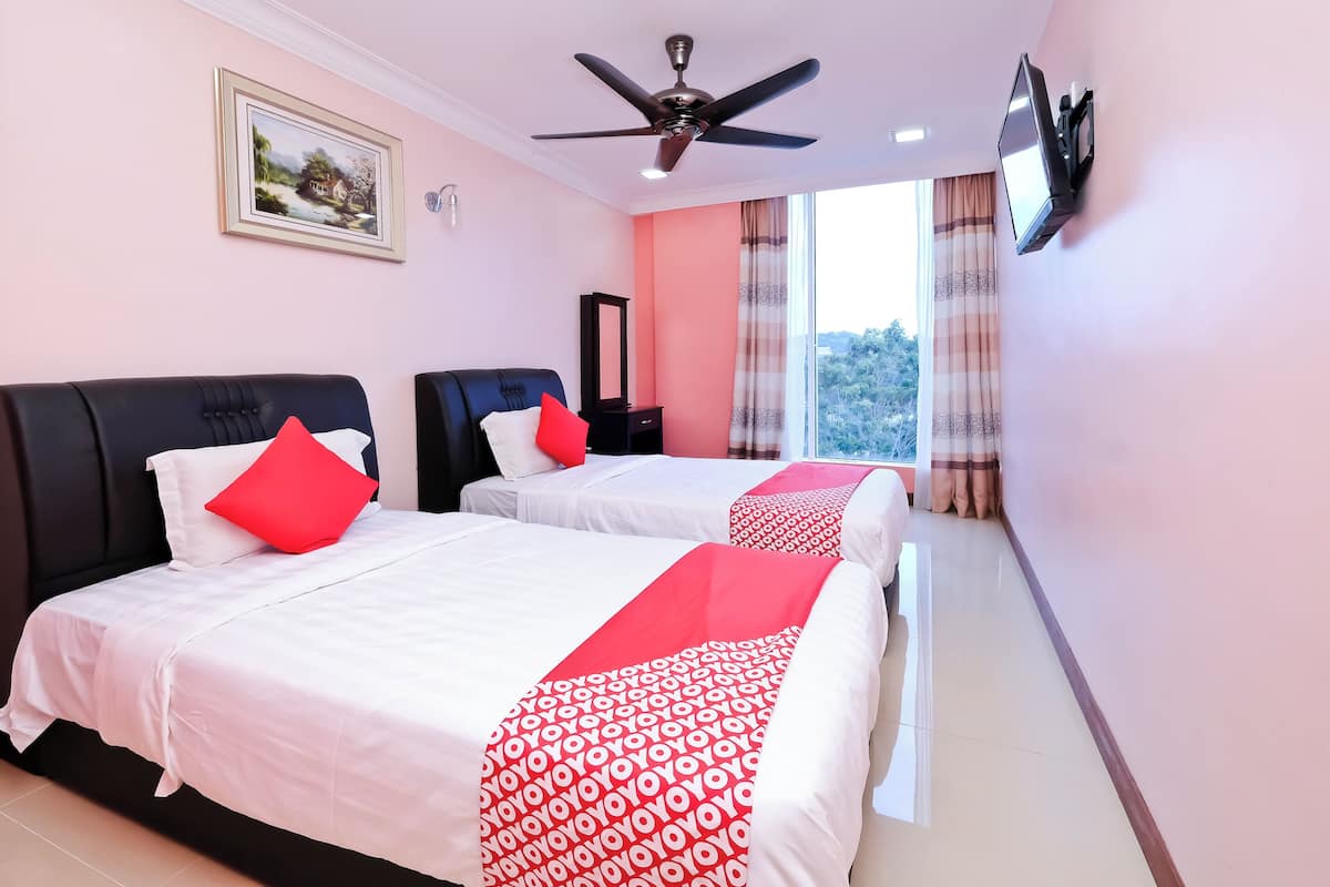 Ein Hotelzimmer mit zwei Betten, einem Deckenventilator, einem an der Wand befestigten Fernseher und einem großen Fenster mit Vorhängen.