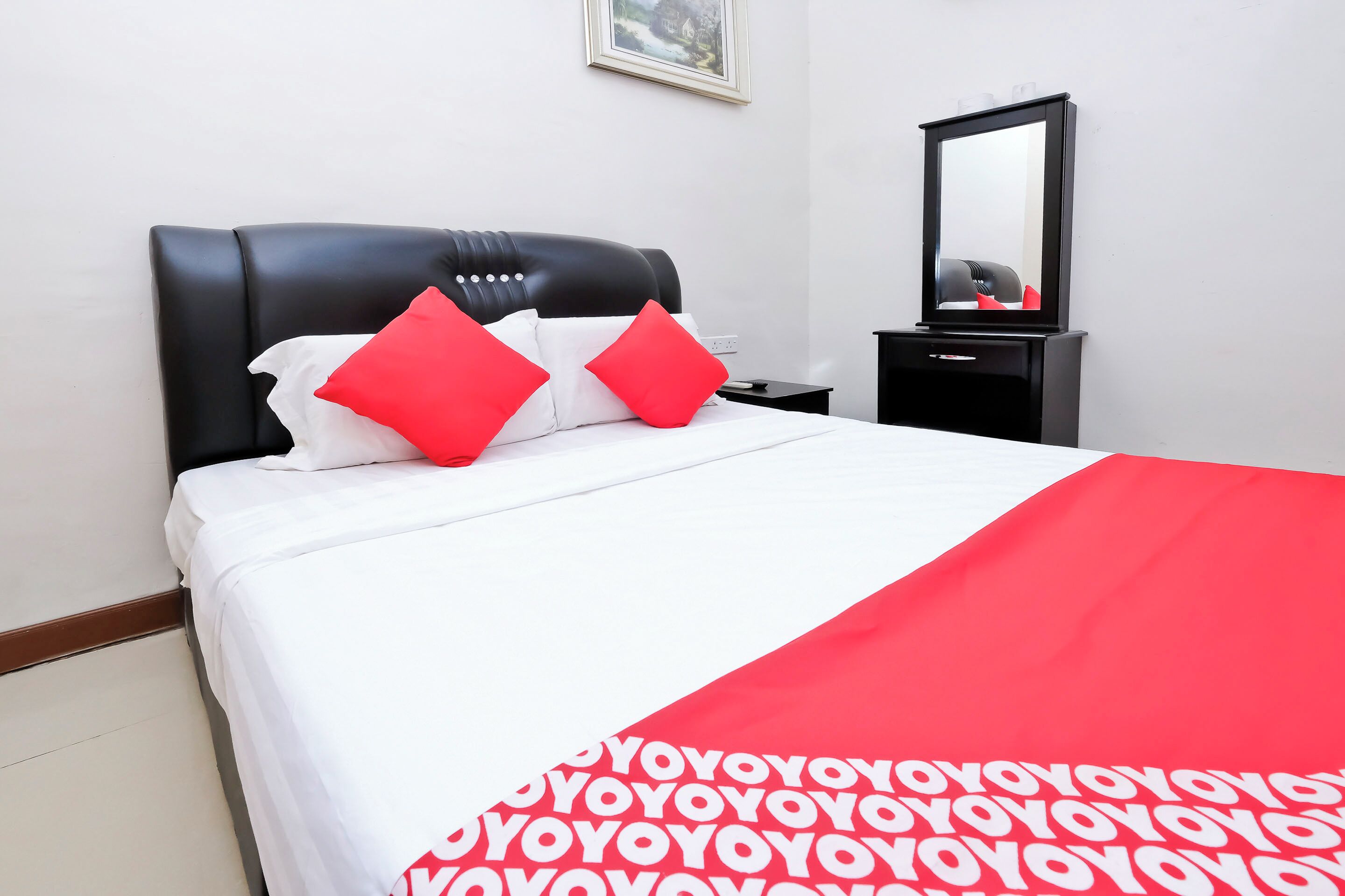 Un lit bien fait, recouvert d’une couverture blanche et rouge, avec une tête de lit noire et deux oreillers rouges.