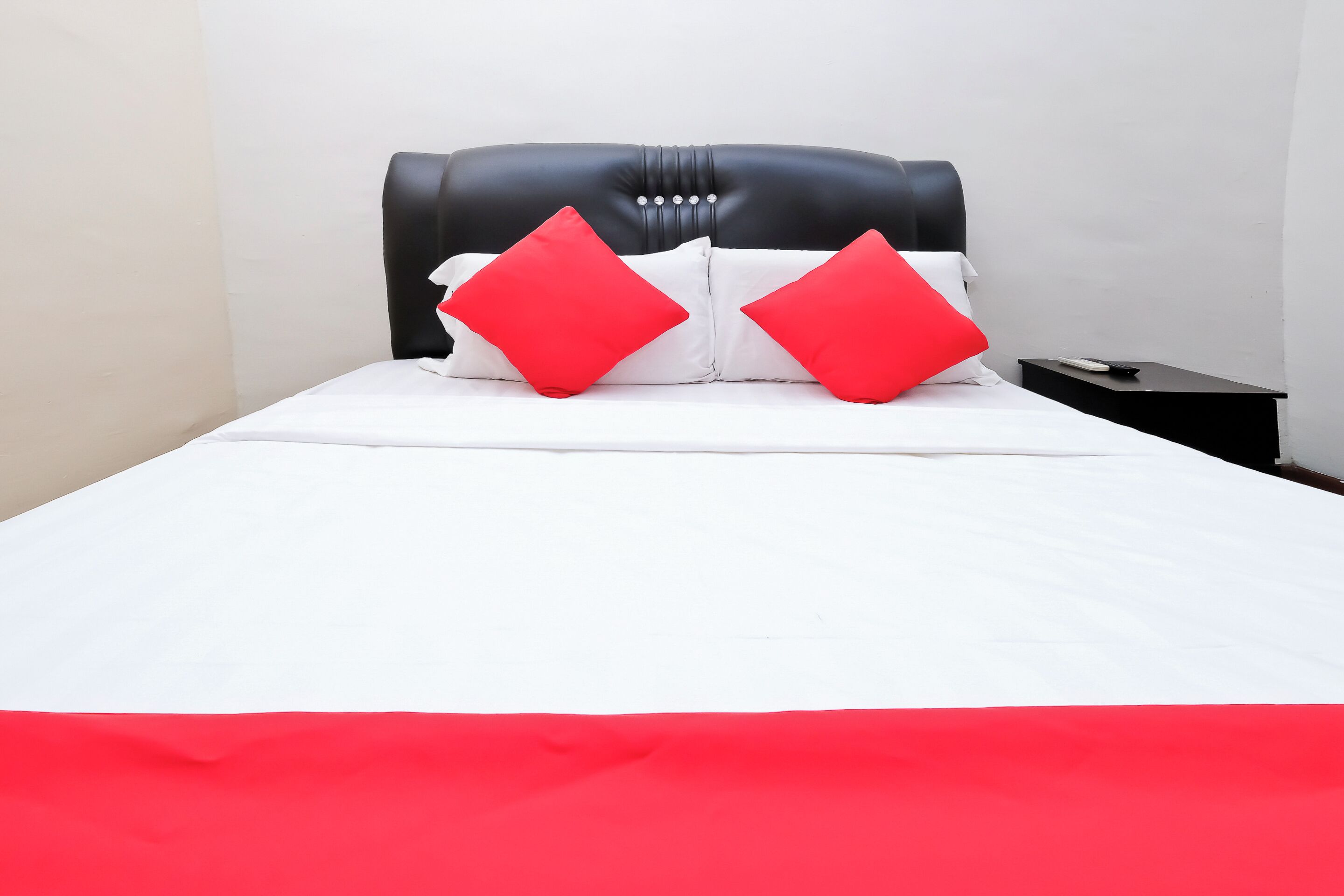 A bed with a black headboard, white bedding, and two red pillows.