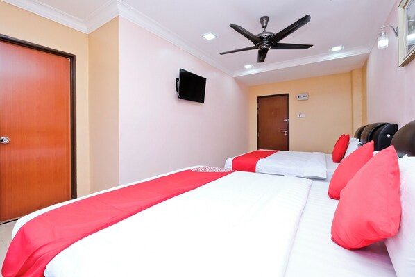A hotel room with two beds, a ceiling fan, a TV, and a door.