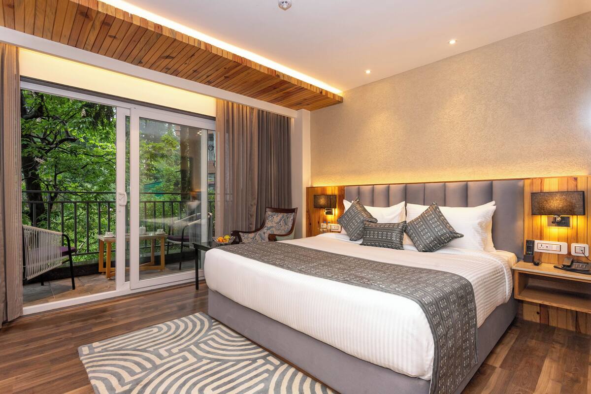 Ein modernes Hotelzimmer mit einem großen Bett, einem Balkon mit Blick auf Bäume und einer Holzbalkendecke.