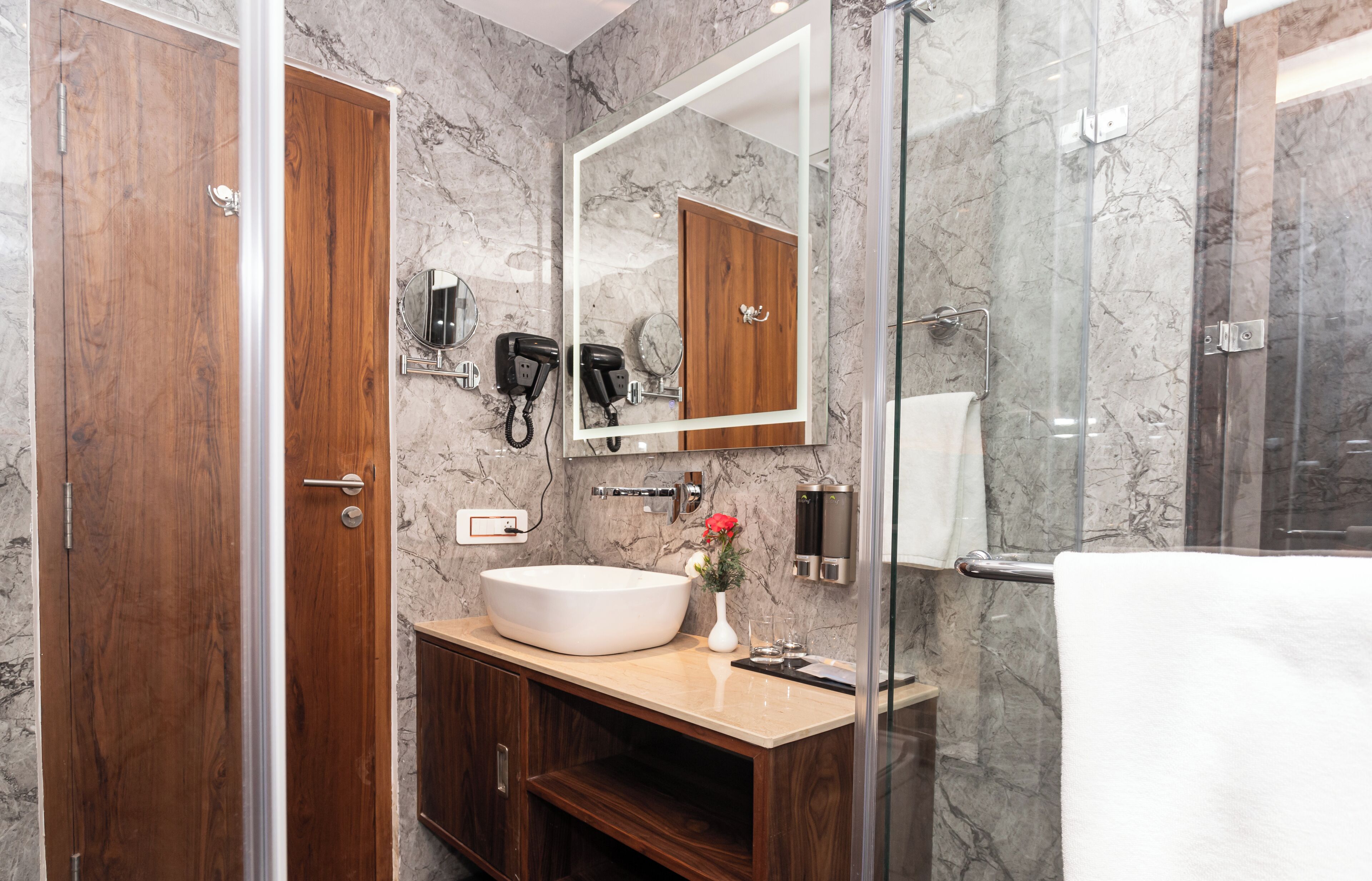 Un baño moderno con un espejo grande, tocador de madera y cabina de ducha de vidrio.