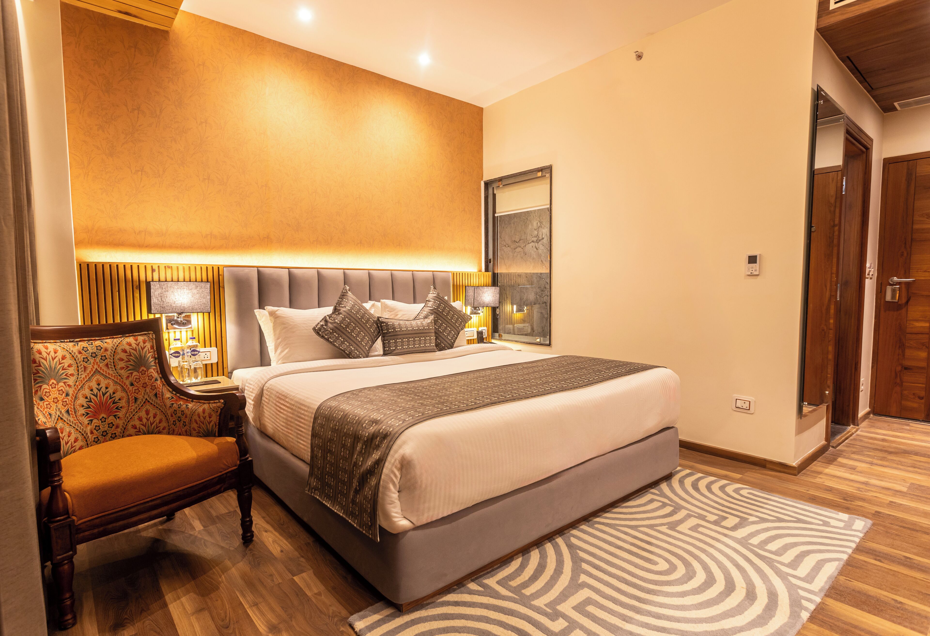 Ein Hotelzimmer mit einem großen Bett, einem Nachttisch, einem Sessel und Holzboden.