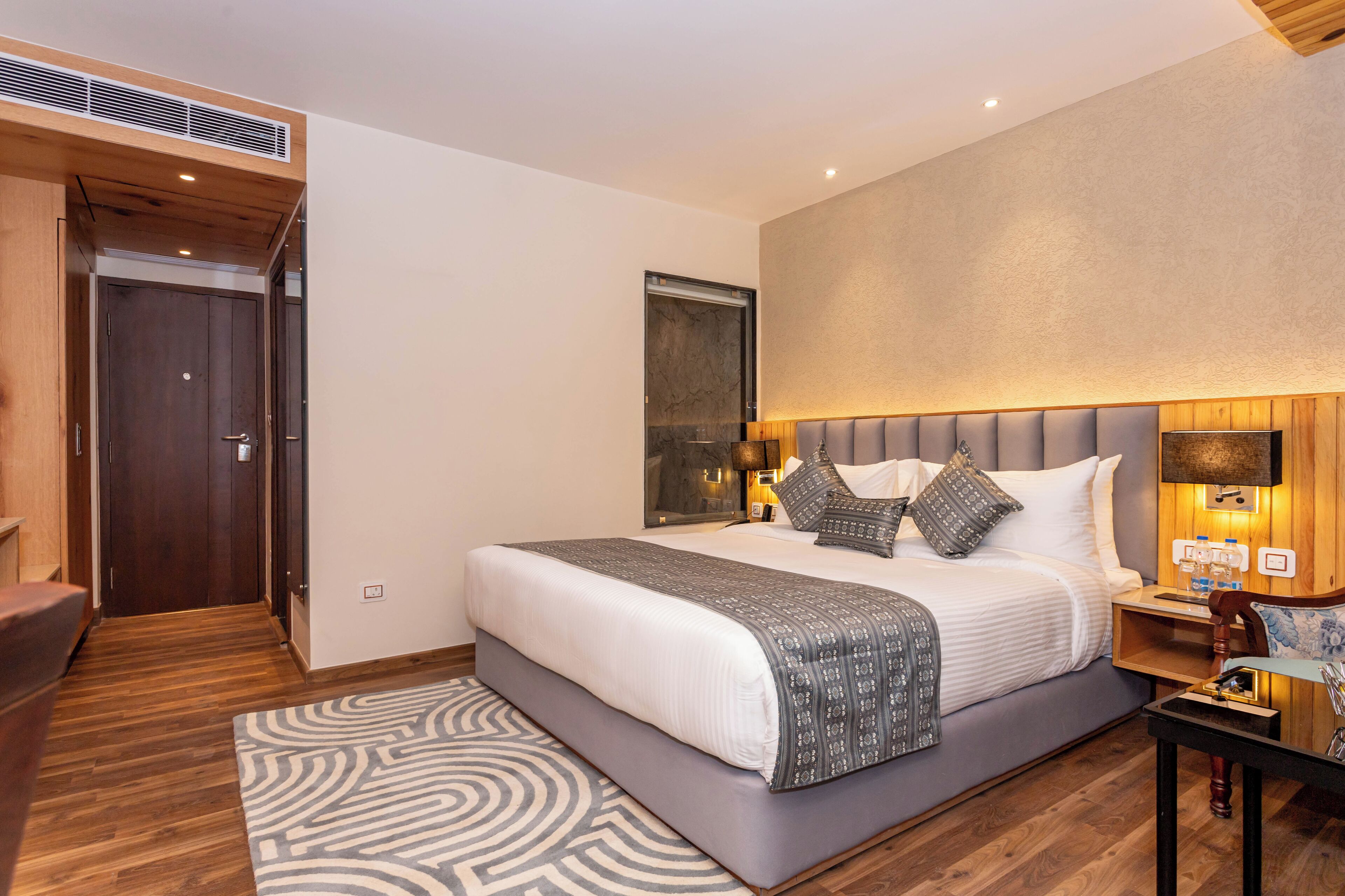 A modern bedroom with a large bed, wooden flooring, a headboard with integrated lighting, and a built-in wardrobe.