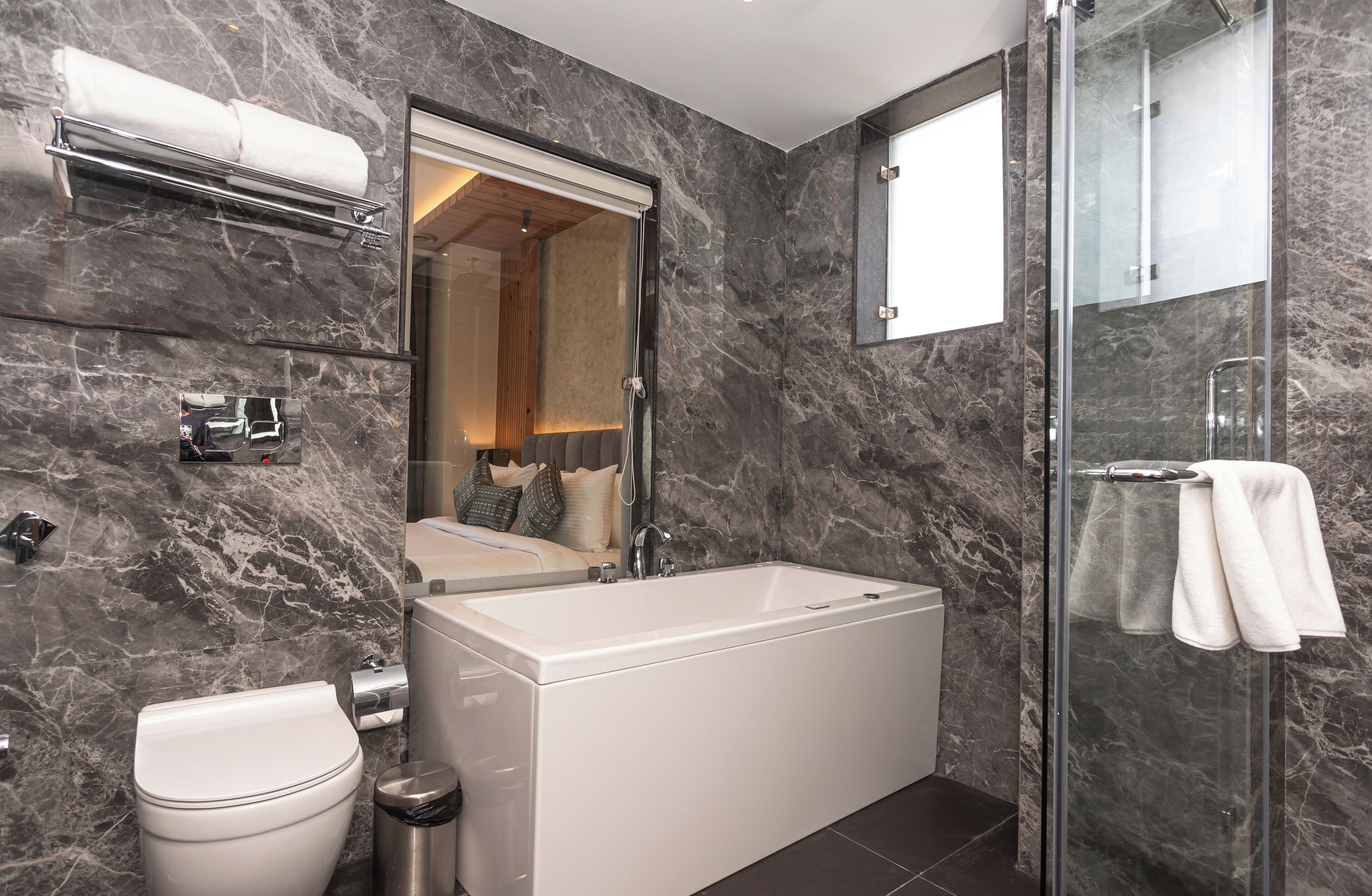 A modern bathroom with a marble wall, a bathtub, a toilet, and a glass shower enclosure.