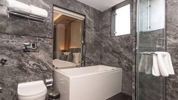 A modern bathroom with a marble wall, a bathtub, a toilet, and a glass shower enclosure.