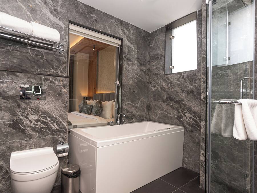 A modern bathroom with a marble wall, a bathtub, a toilet, and a glass shower enclosure.