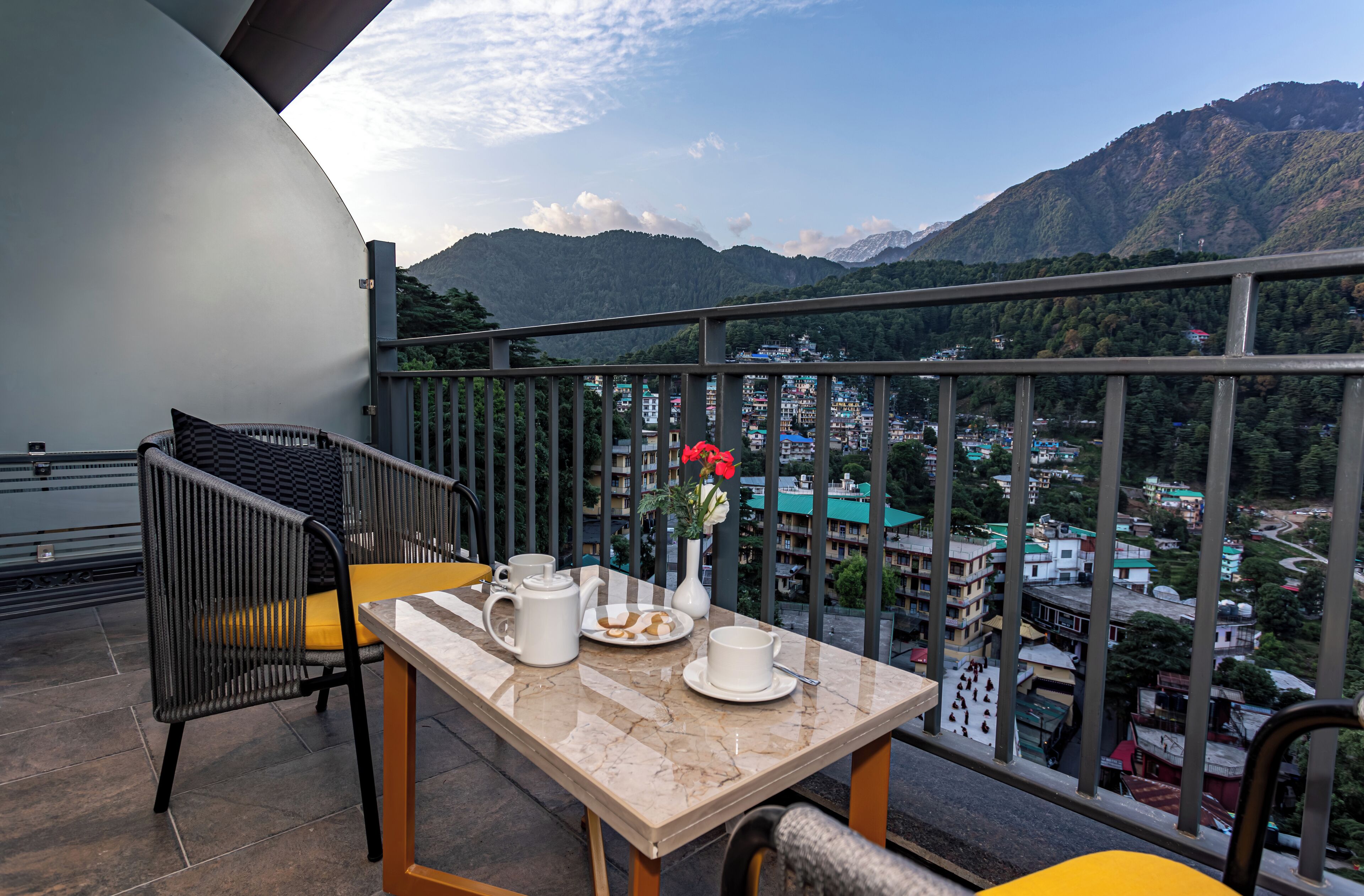 A balcony with a table set for tea, a chair, and a view of a mountainous landscape.