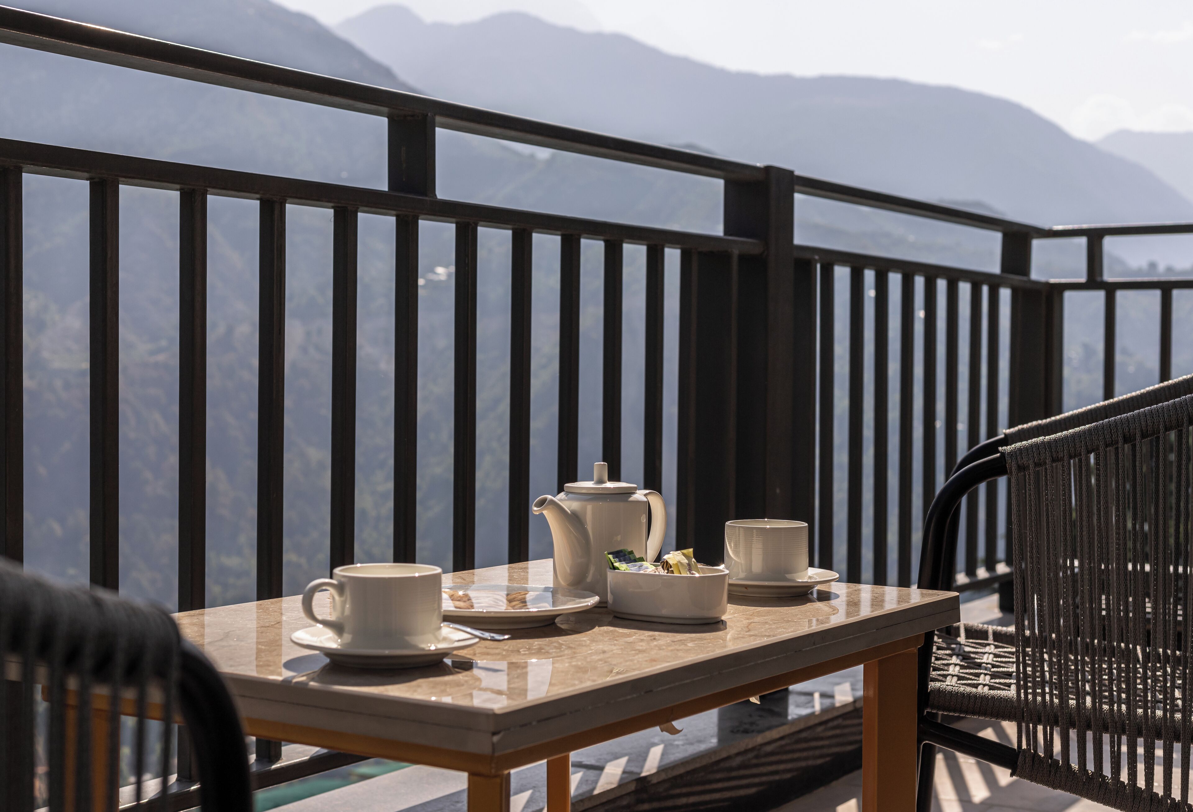 A balcony with a table set for tea, a chair, and a view of mountains.