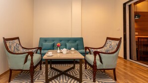 A room with a blue sofa, two wooden chairs, a table with a vase, teapot, and cups.