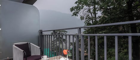 A balcony with a table set for two, featuring a white teapot, cups, and a vase with flowers.